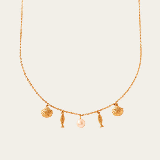 Gold necklace with shell and fish charms on a beige background