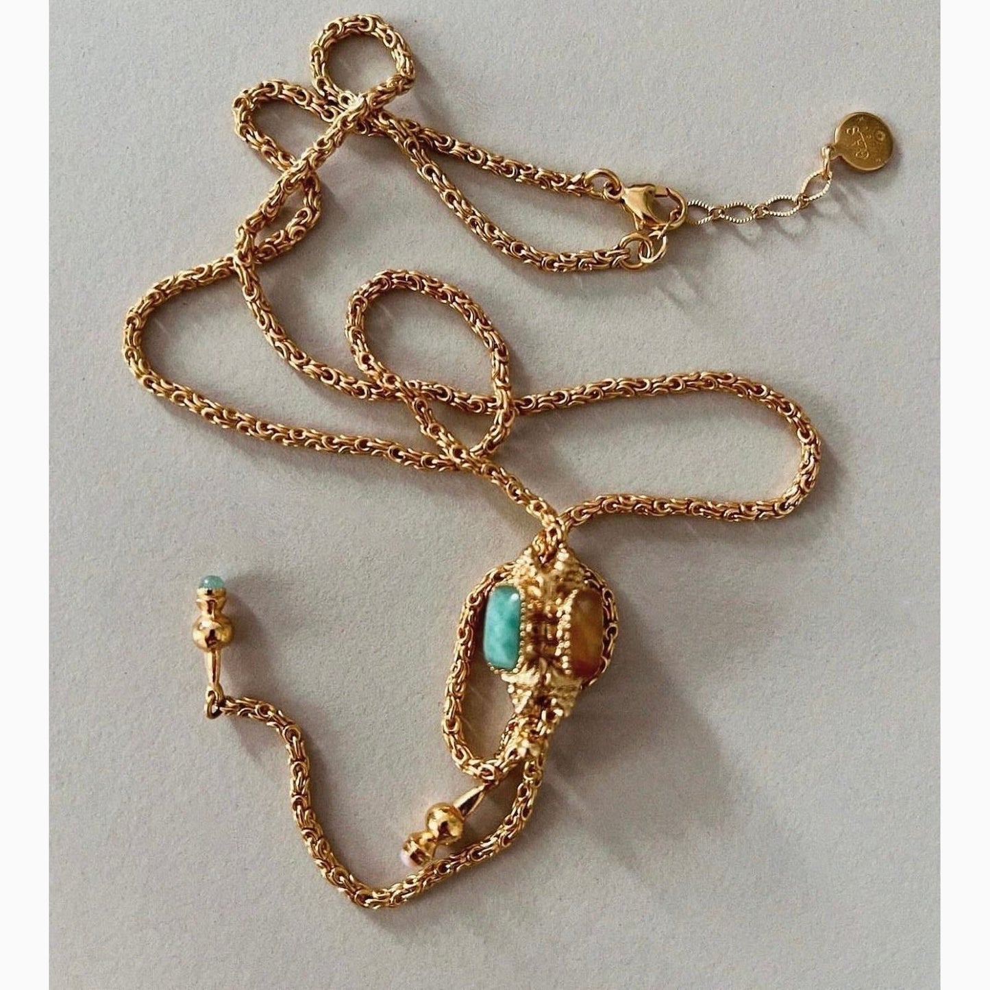 Long gold necklace with coloured talisman on neutral background