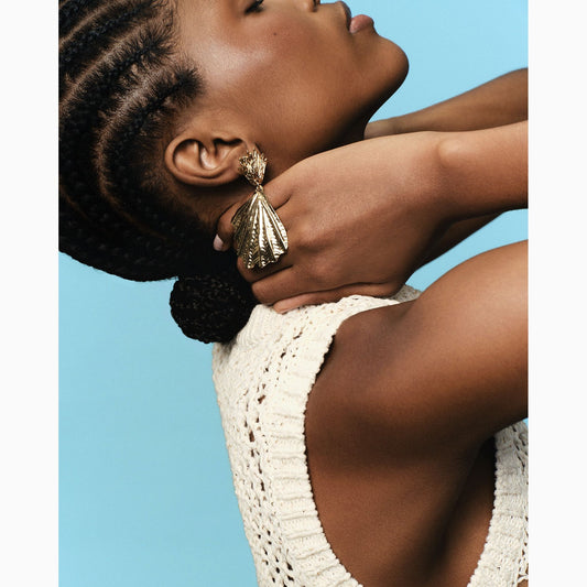 Woman wearing a white crochet top against a blue background and silver shell drop earrings