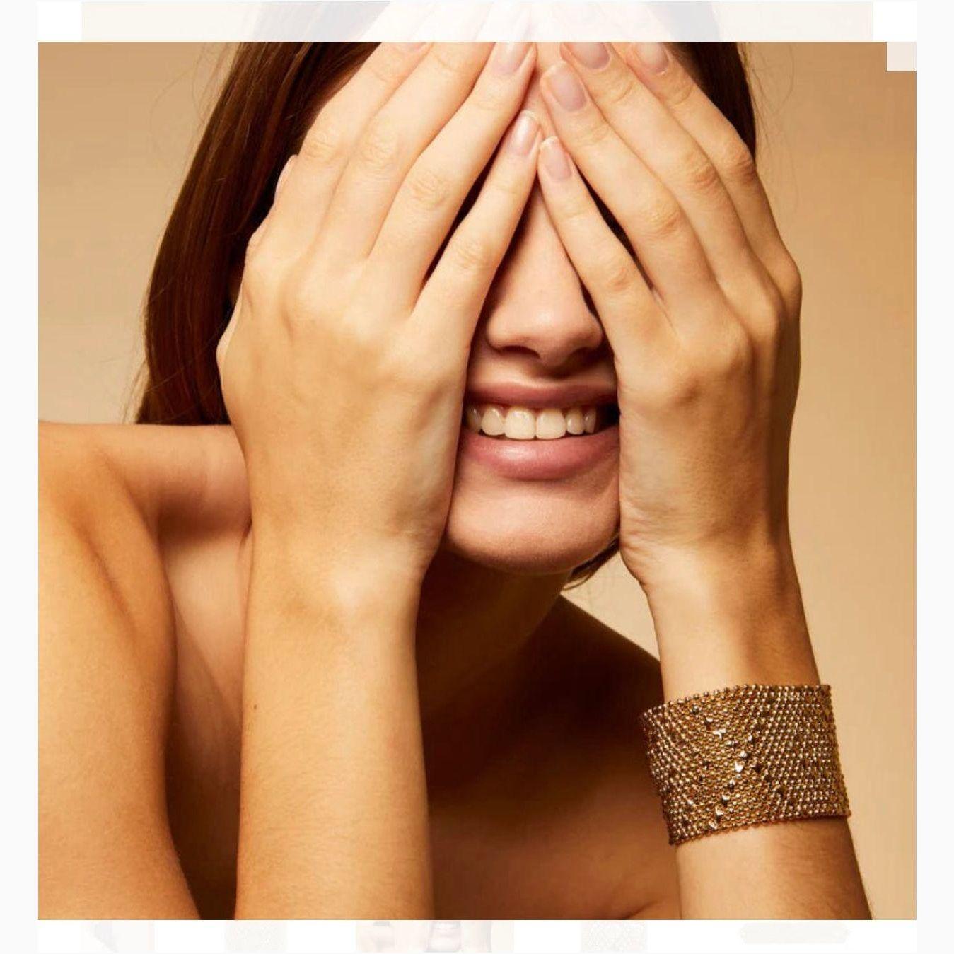 A person covering their face with their hands, showcasing a gold-plated cuff bracelet with multiple chains and star-shaped accents on the wrist.