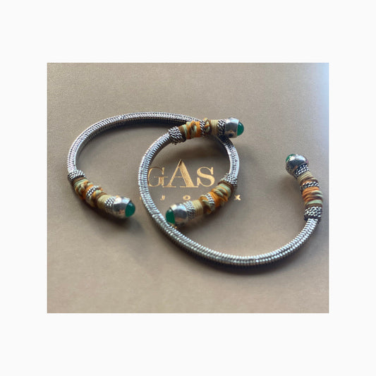 two silver bangles on a gas bijoux gift box, each have green stones at the ends and wrapped partially with coloured threads