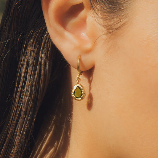 Gold hoop earring with a green gemstone close up on woman