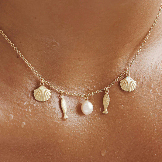 Necklace with shell, fish, and pearl charms on a person's neck.