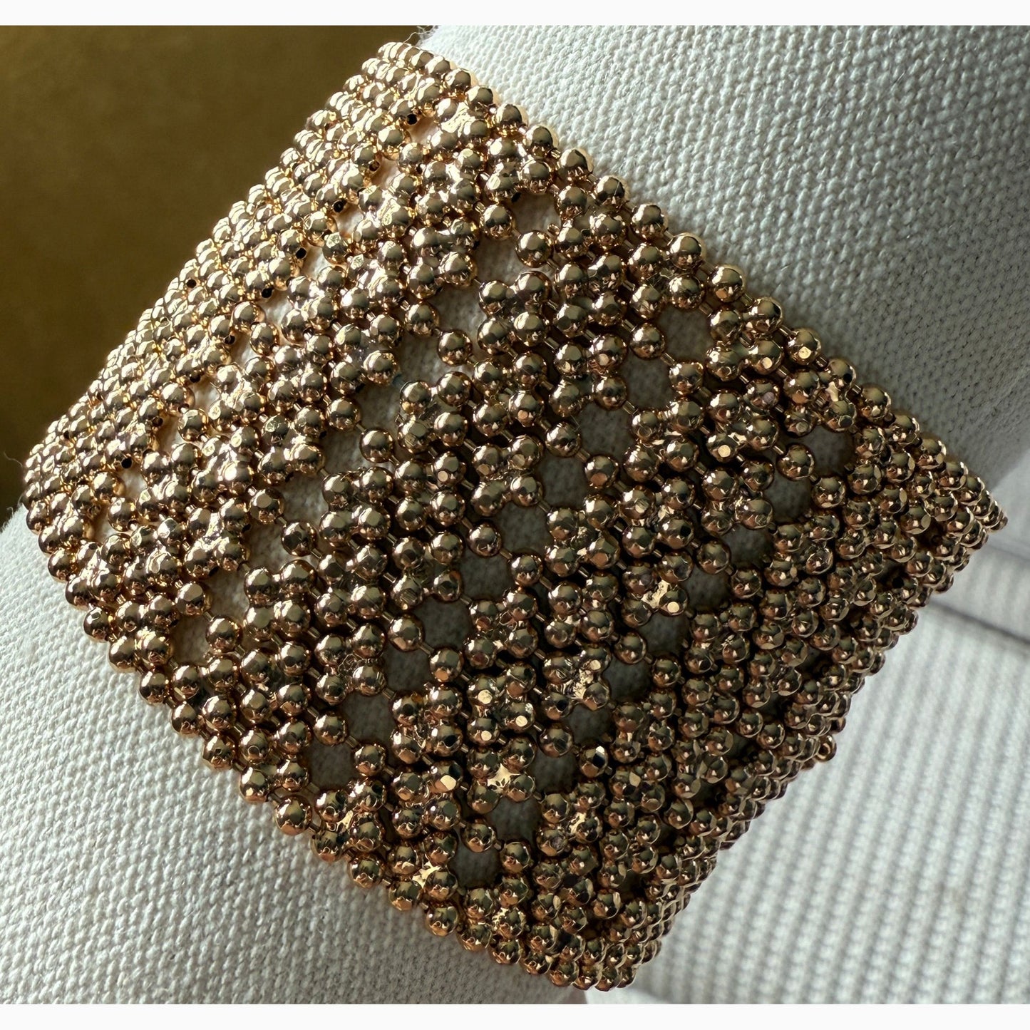 Close-up of a gold beaded bracelet on a white fabric background