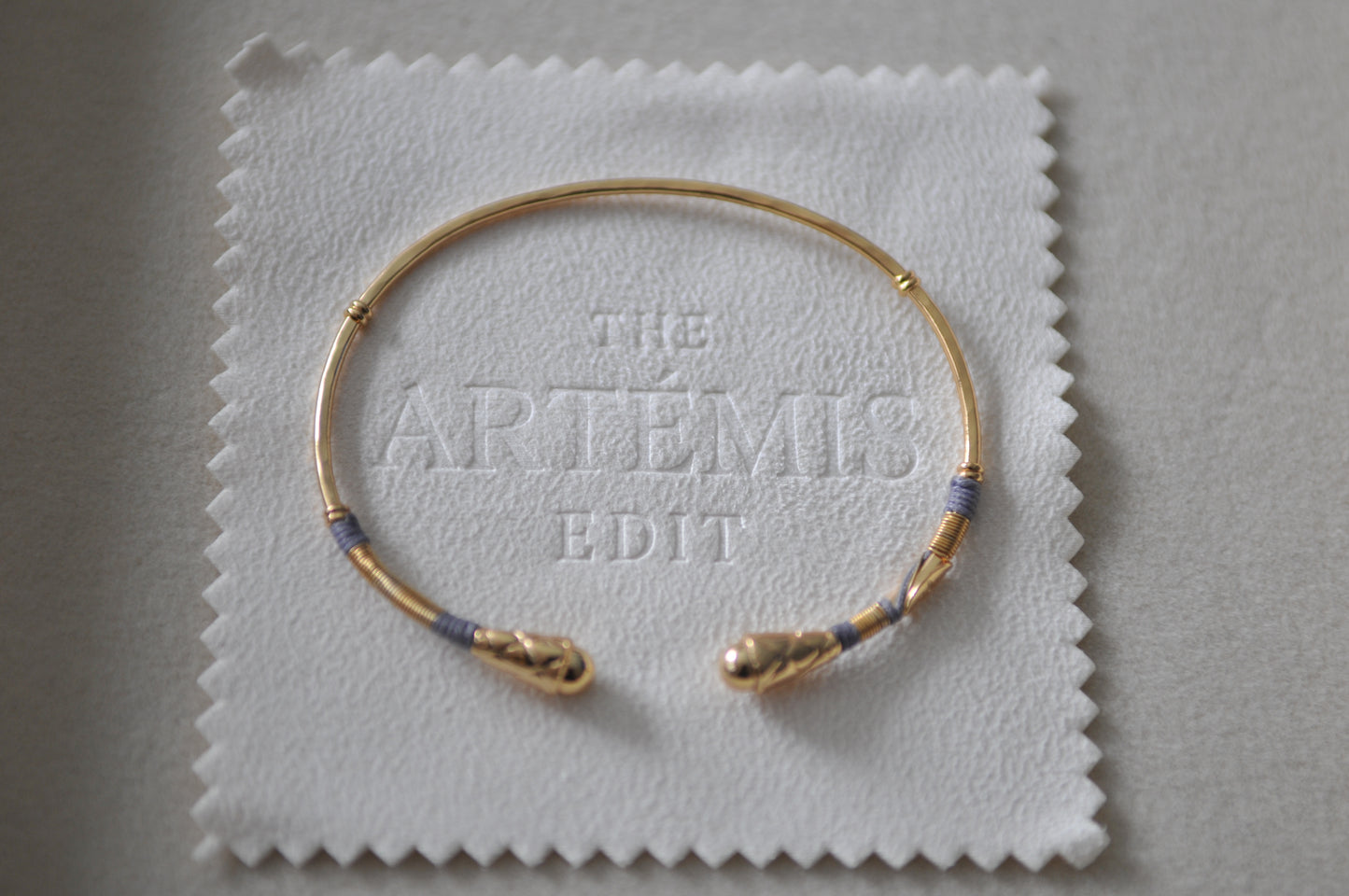 Gold bracelet on a white cloth with 'The Artemis Edit' branding.