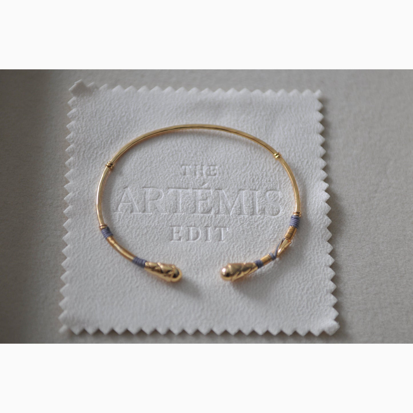 Gold bracelet on a white cloth with 'The Artemis Edit' branding.