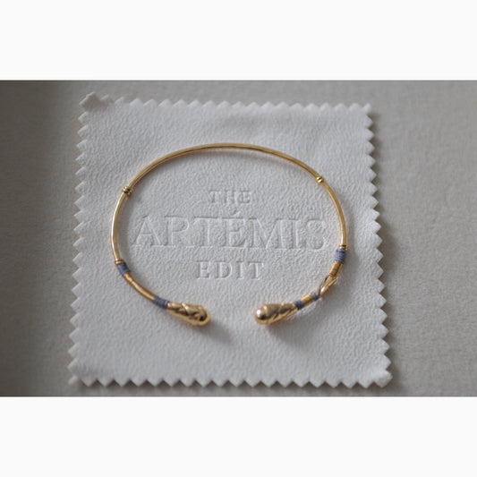 Gold bracelet on a white cloth with 'The Artemis Edit' branding.