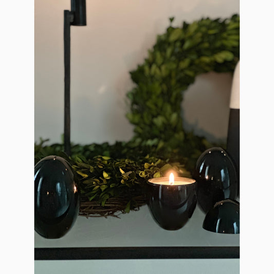 Black omorfi candle lit, with decorative wreath in background