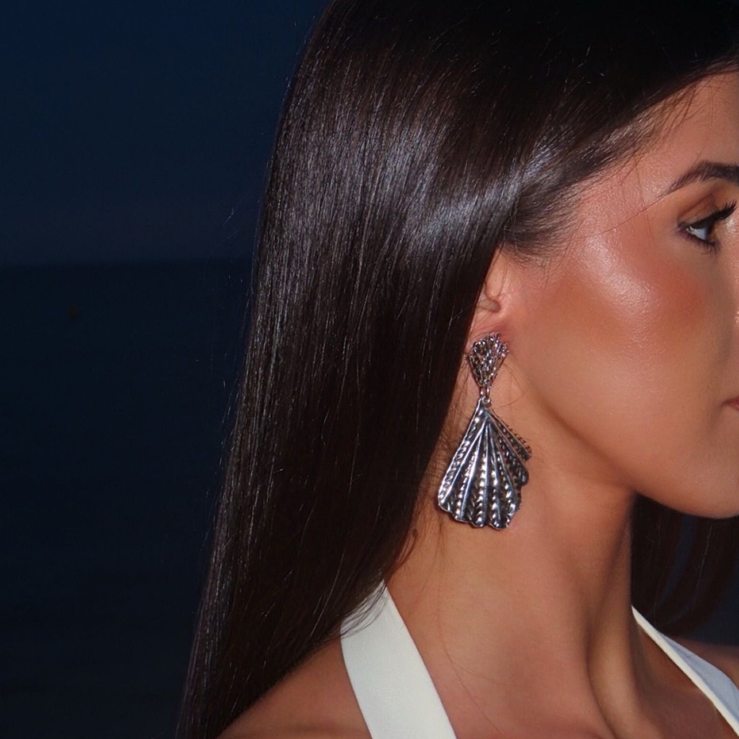 Woman wearing large silver earrings with a dark background