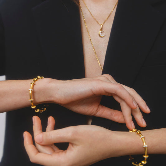 Close-up of a person wearing gold jewelry including a necklace, bracelet, and ring.