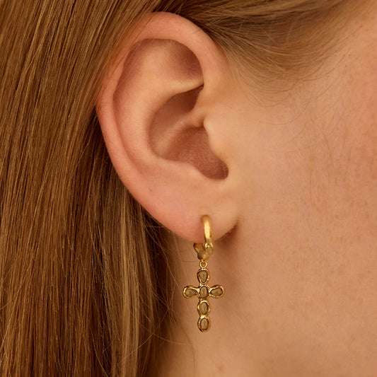Gold cross earring worn by a person with brown hair.