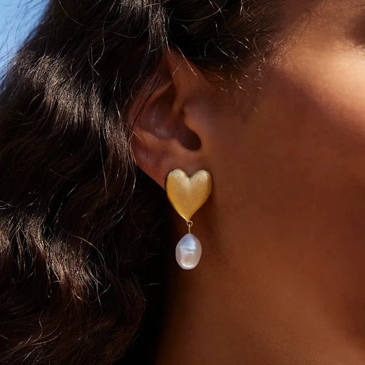 Heart-shaped earring with a pearl drop worn by a person.