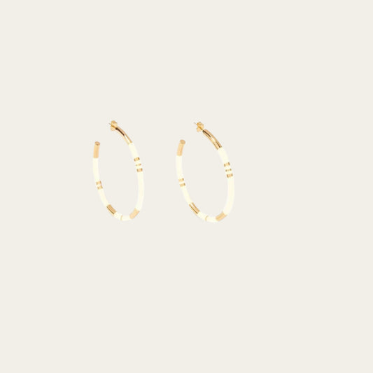 Aurélie Bidermann Positano earrings, featuring ivory-colored stripes in resin and gilded with 750/1000 yellow gold. On flat lay neutral