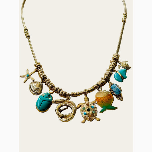 Necklace with various charms including a turtle, shell, and scarab on a neutral surface