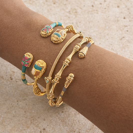 Gold bracelet with colorful accents on a wrist against a neutral background.