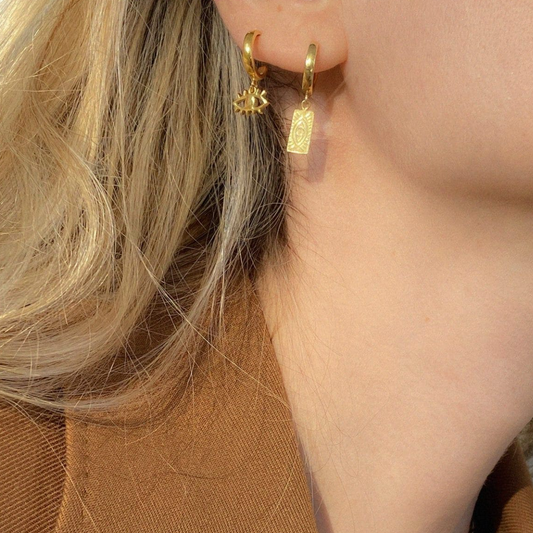 Close-up of a person wearing gold hoop earrings with star and bar designs.