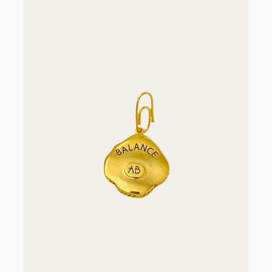 Gold pendant with 'BALANCE' and 'AB' engraved on a light gray background