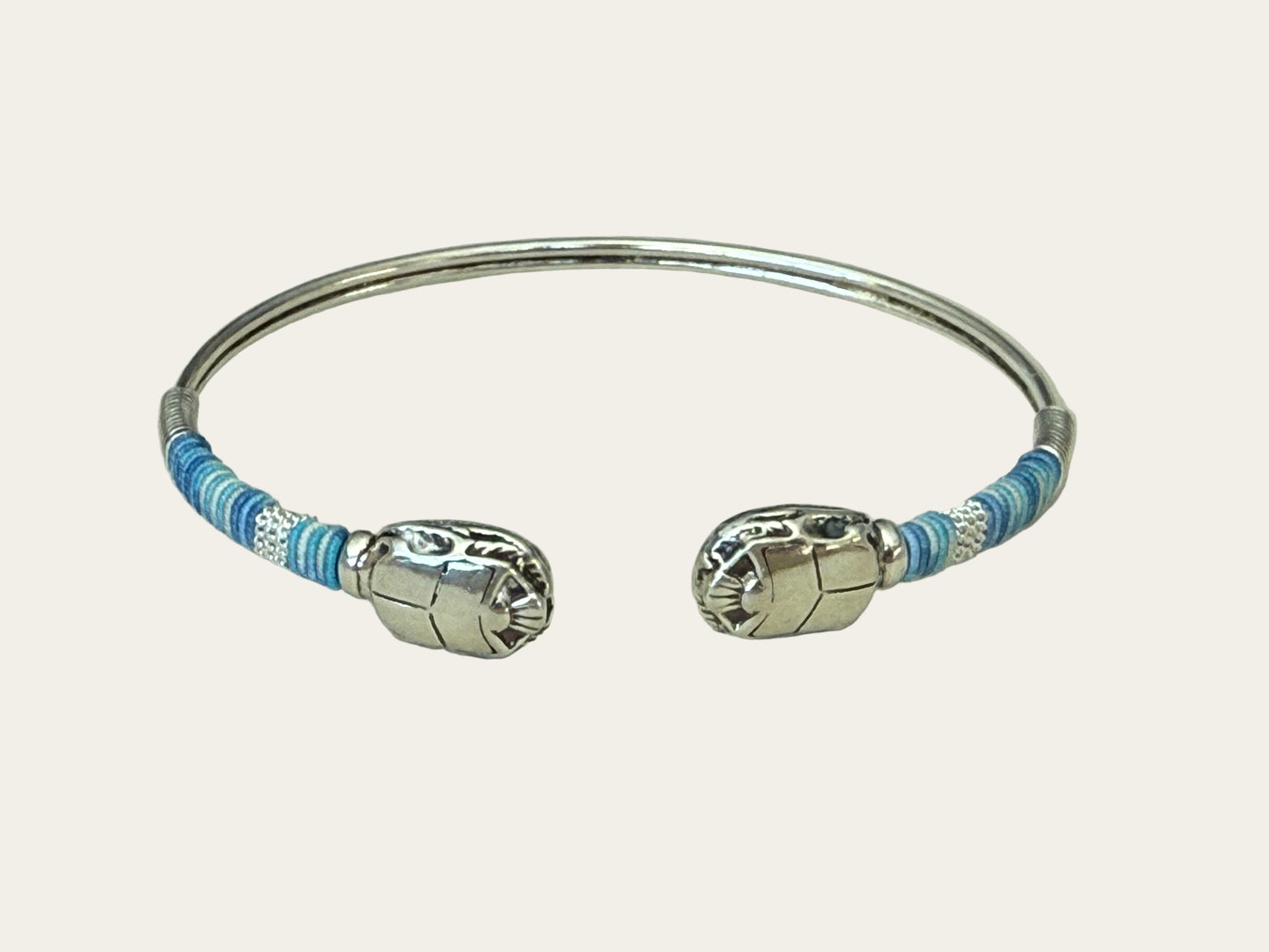 Silver bracelet with blue threads on a light gray background
