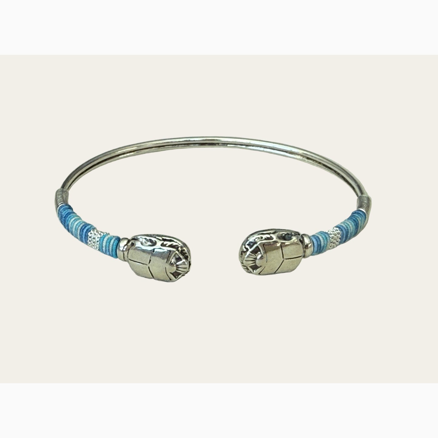 Silver bracelet with blue threads on a light gray background