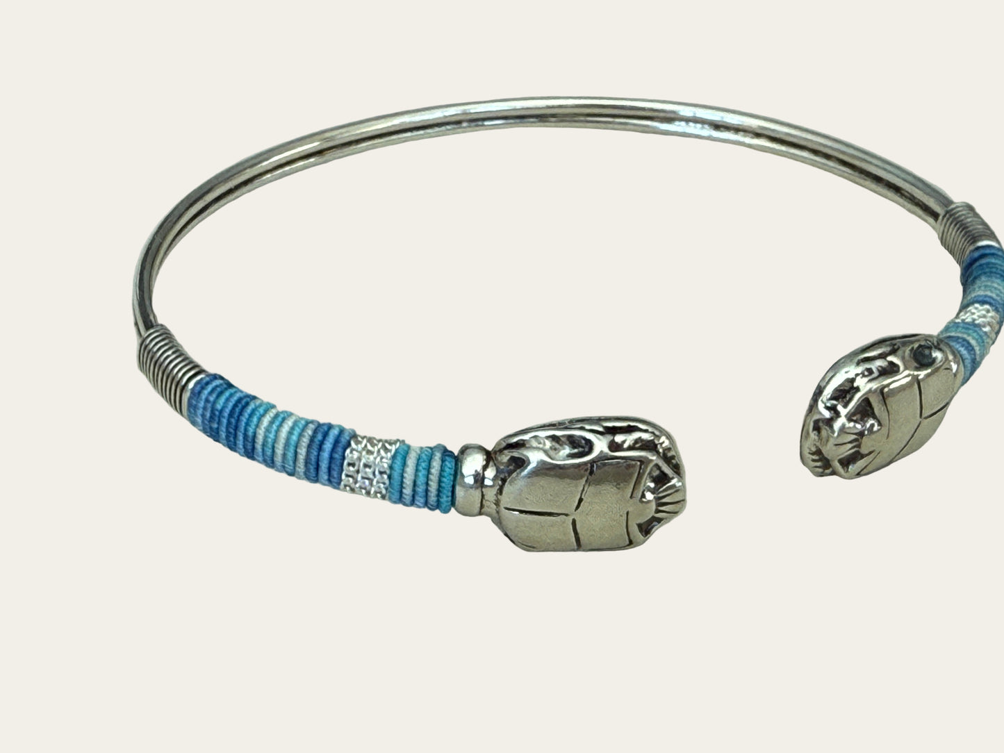 Silver bracelet with blue and white striped threads on a light gray background
