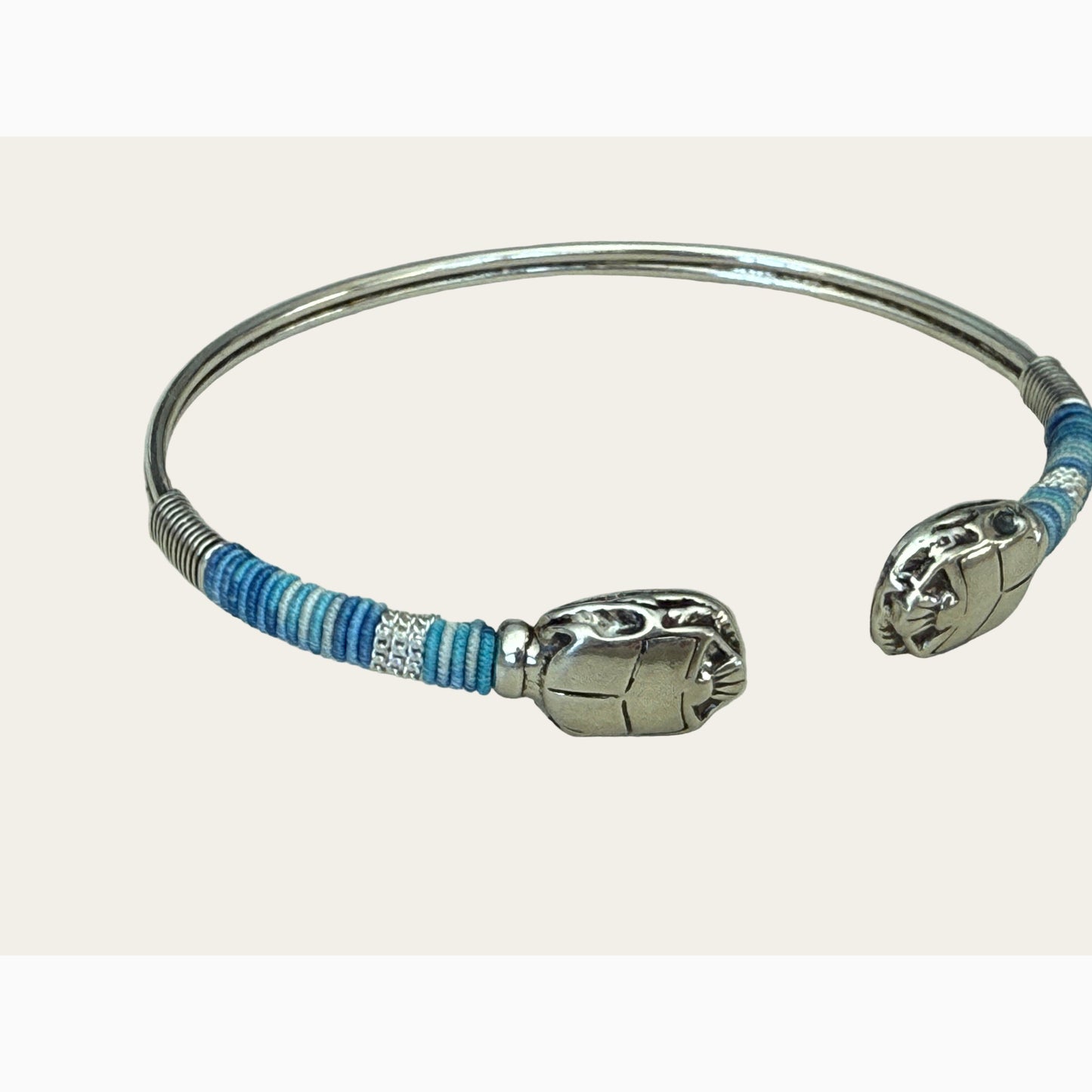 Silver bracelet with blue and white striped threads on a light gray background