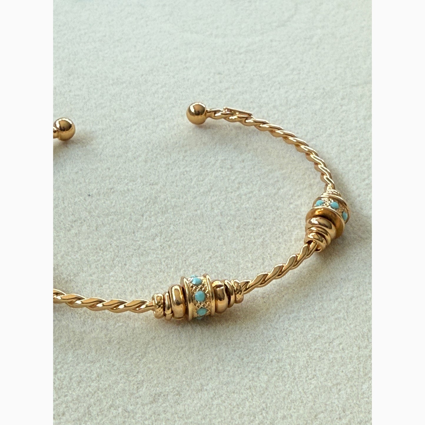 Gold bracelet with turquoise stones on a light gray background