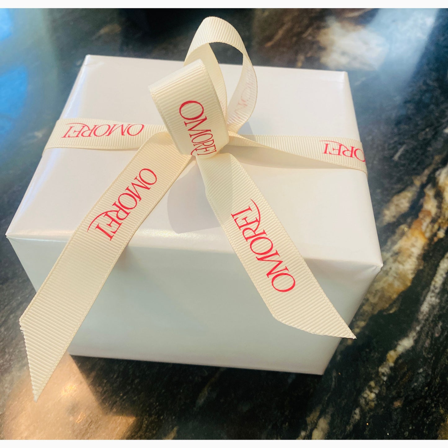 White gift box with a beige ribbon tied in a bow on a dark surface
