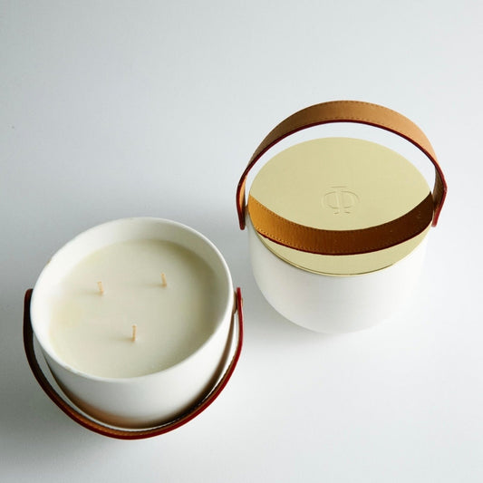 Two candles in white containers with brown handles on a light gray background