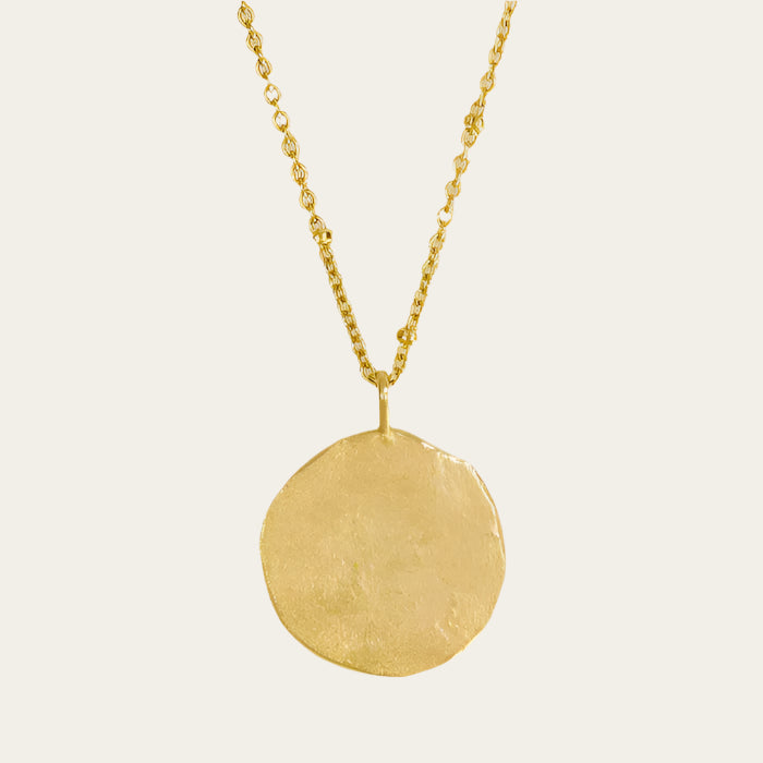 A gold-plated hammered full moon pendant necklace displayed on a mannequin.