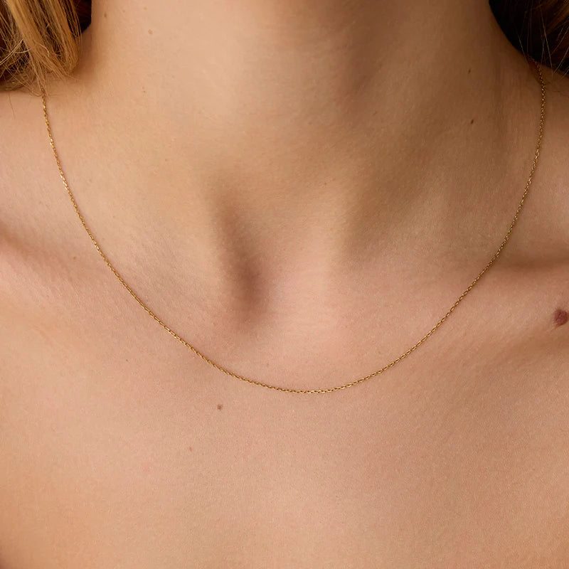 Gold necklace on a person's neck against a neutral background