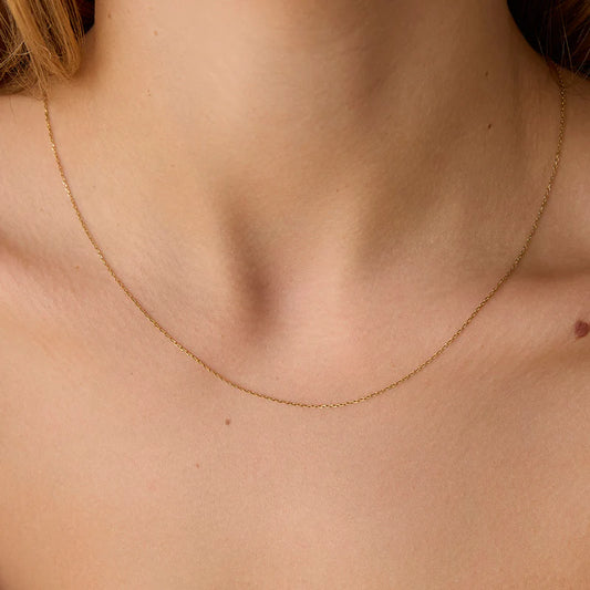 Gold necklace on a person's neck against a neutral background