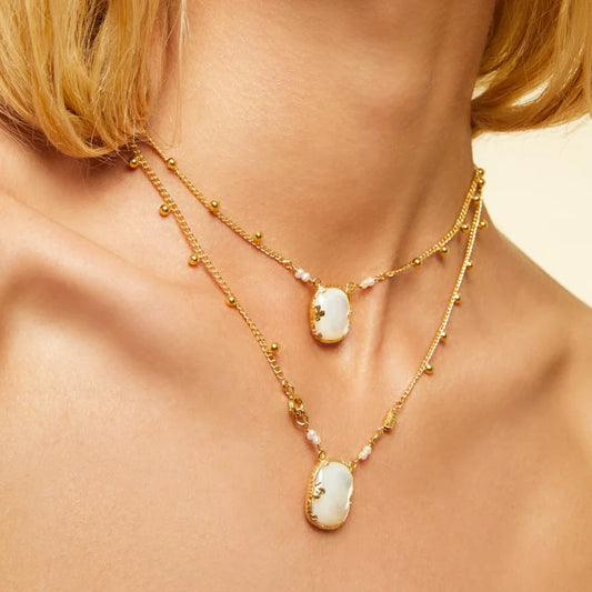 Gold necklaces with stone pendants on a person's neck