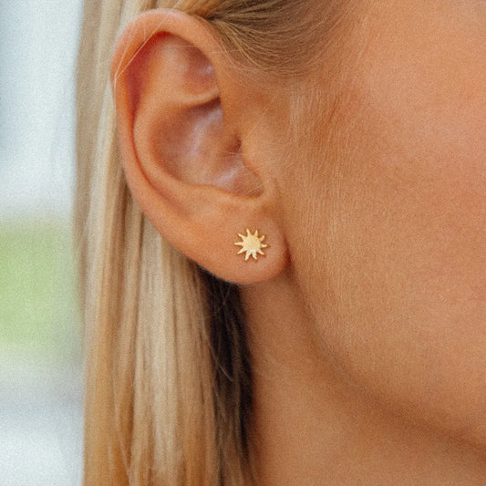 sun burst gold studs close up on womans ear