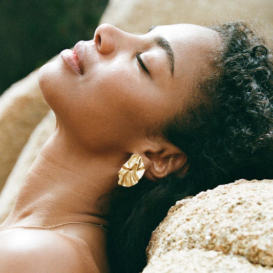 Gold Earrings on woman with rocky background