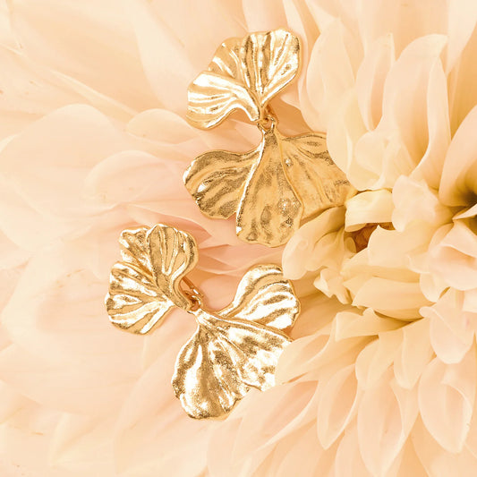 Gold leaf-shaped earrings on a soft peach-colored floral background