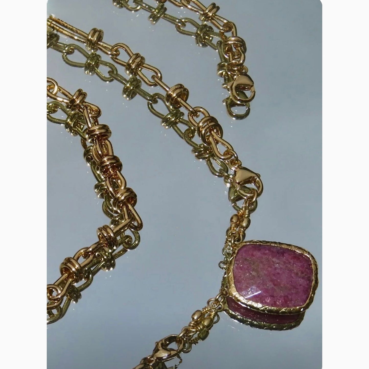 Gold chain necklace with a stone pendant on a reflective surface