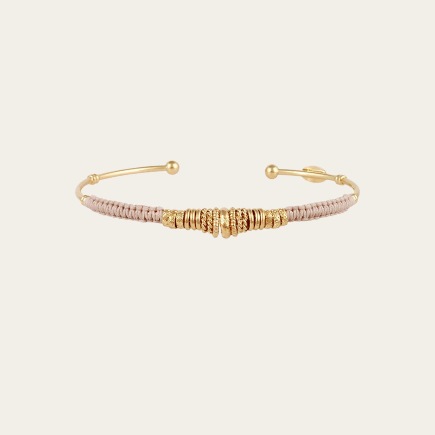 gold bangle with coloured threads and gold rings on neutral background