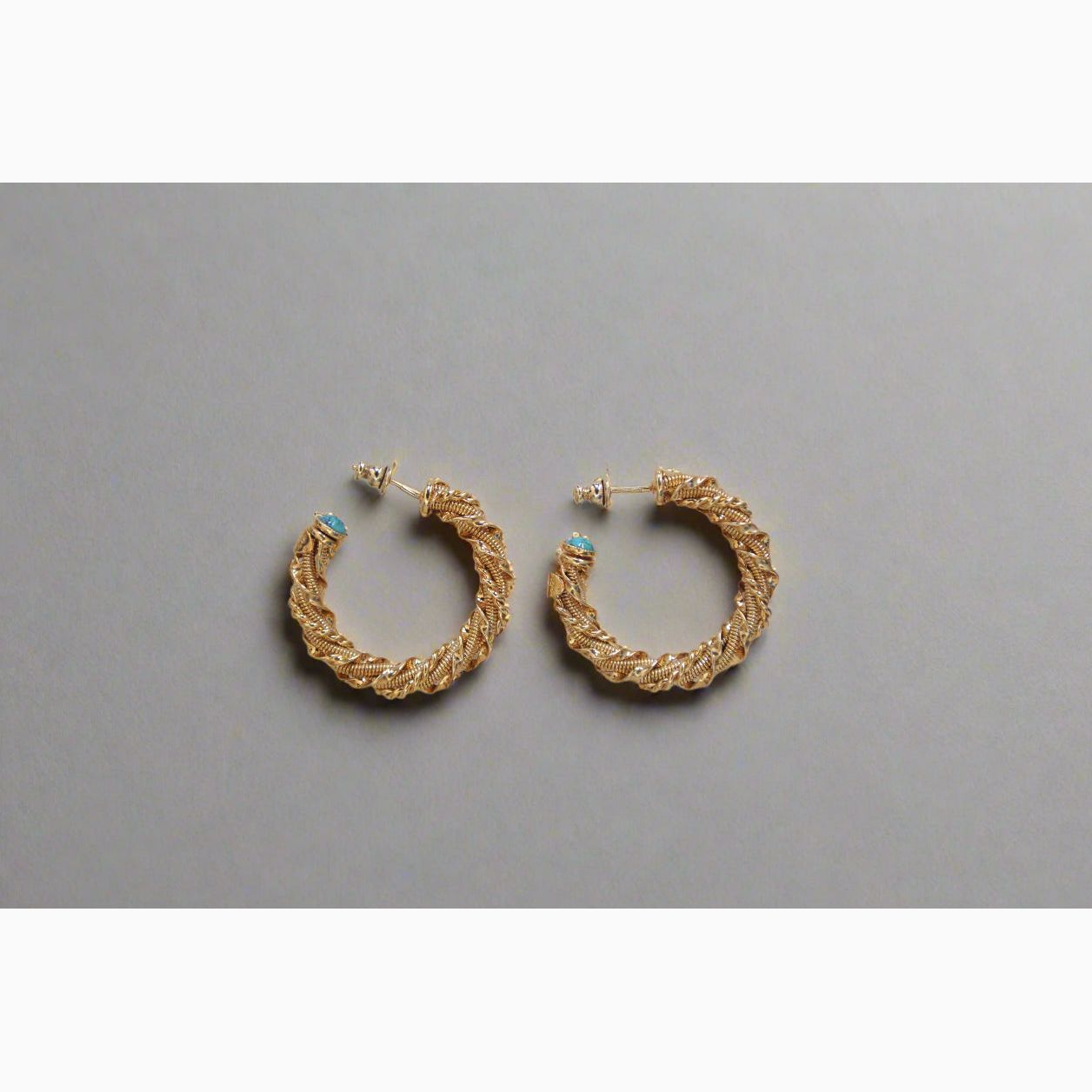 Gold braided hoop earrings with turquoise stones on a grey background
