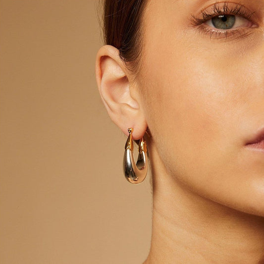 Gold hoop earrings worn by a model against a beige background