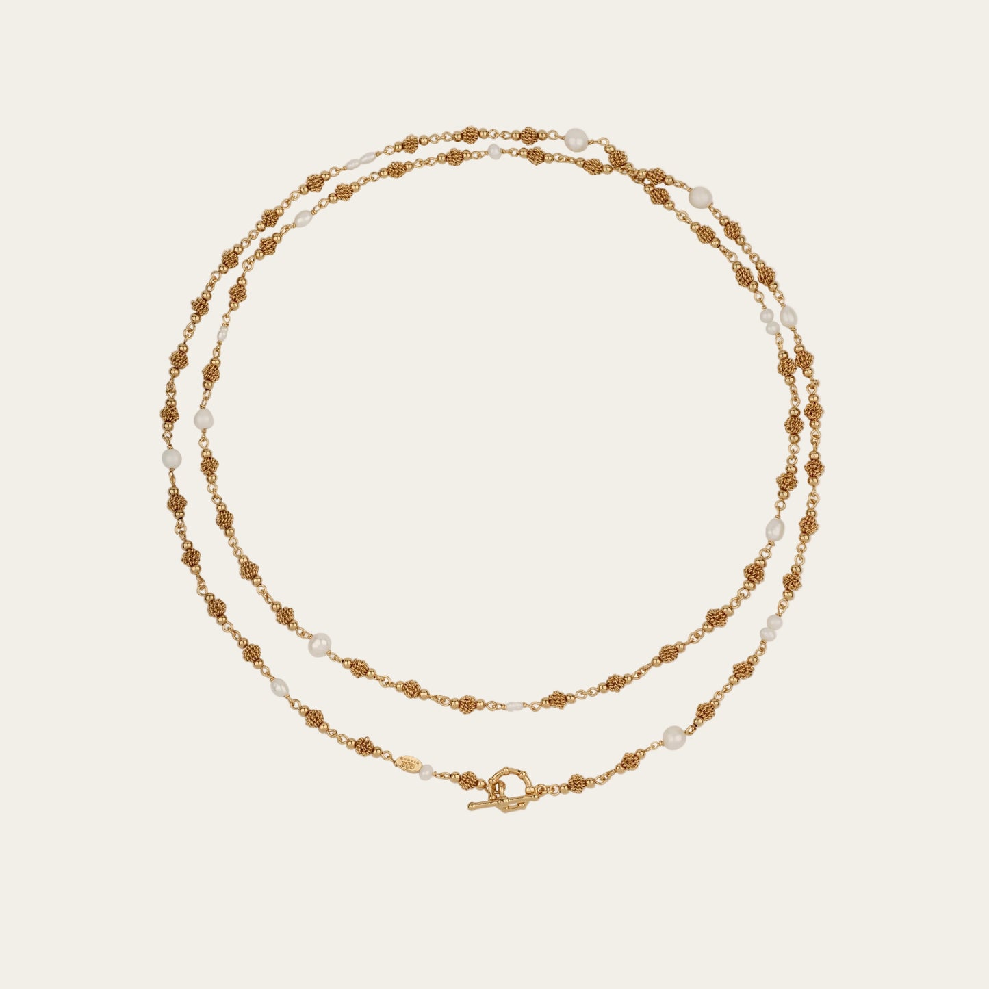 Long gold necklace with small pearls on a light beige background