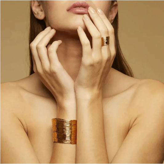 A woman wearing a gold-plated bracelet with a stacked metallic thread design on her wrist.