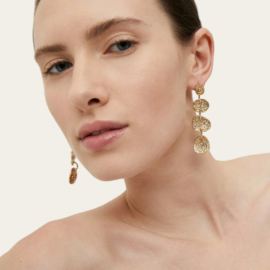 Model wearing Gas Bijoux Éclipse Strass gold-plated drop earrings with hammered linked discs and clear strass detailing, with hair swept back.