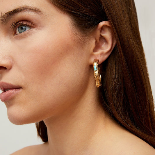 Close-up of a woman wearing gold hoop earrings with a gemstone on a neutral background