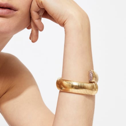 Gold bracelet on a person's wrist with a neutral background