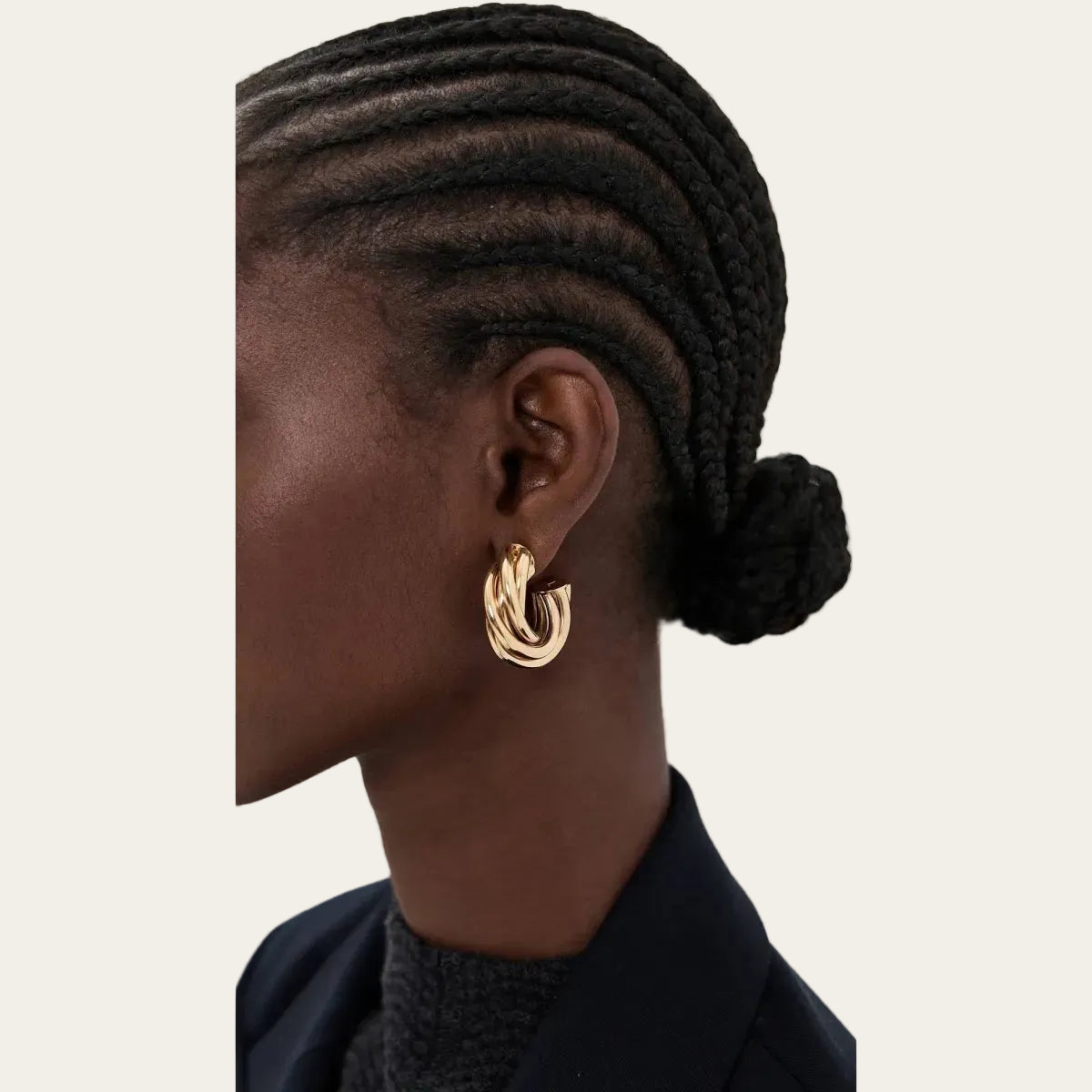 Close-up of an ear wearing a gold hoop earring with braided hair on a neutral background