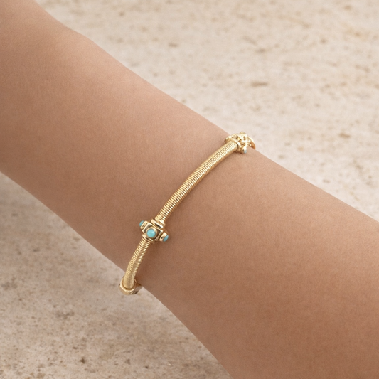 Gold bracelet with a turquoise stone on a wrist against a beige background