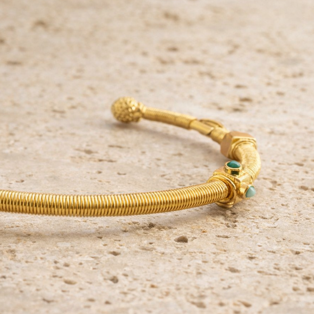 Gold bracelet with small green stones on a beige surface