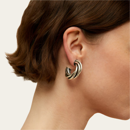Close-up of a person wearing a silver hoop earring on a neutral background
