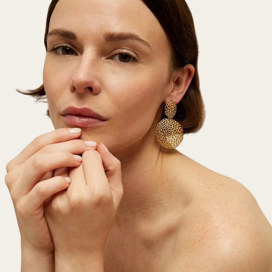 Model wearing Gas Bijoux Onde Gourmette gold-tone drop earrings with circular openwork chain motifs, with hair tucked behind the ear.