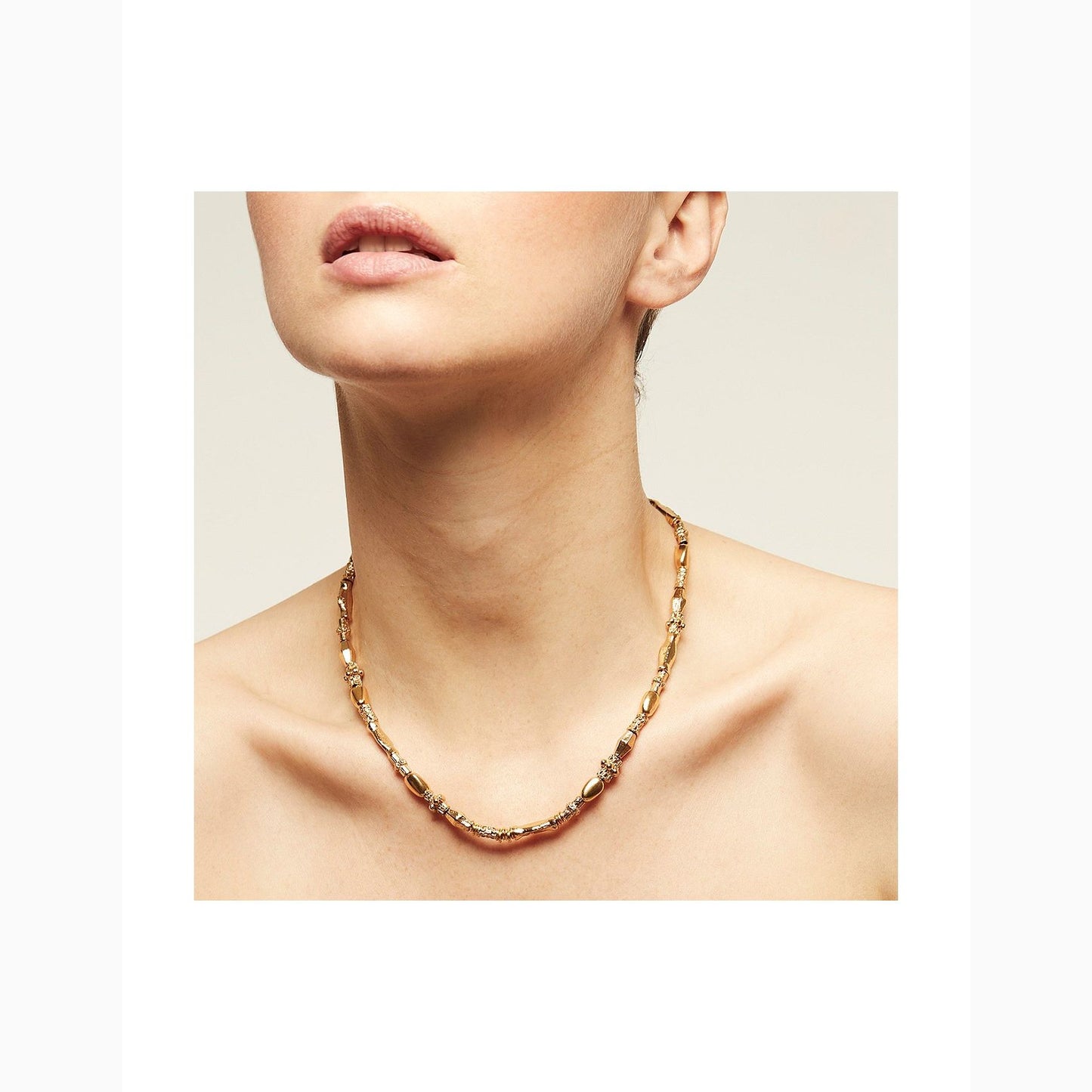 Gold chain necklace worn by a person on a neutral background